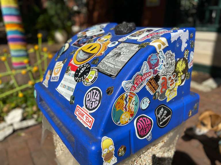 An outdoor trashcan lid covered in stickers